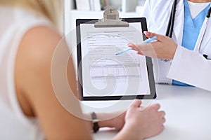 Close up of a doctor and patient hands while phisician pointing into medical history form at clipboard