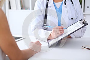 Close up of a doctor and patient hands while phisician pointing into medical history form at clipboard
