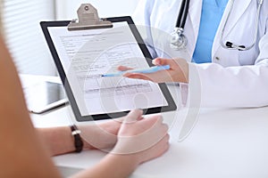 Close up of a doctor and patient hands while phisician pointing into medical history form at clipboard