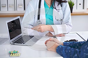 Close-up of a doctor and patient sitting at the desk while physician pointing into laptop computer. Medicine and heal