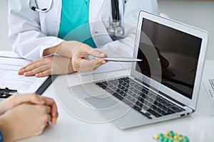 Close-up of a doctor and patient sitting at the desk while physician pointing into laptop computer. Medicine and heal