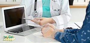 Close-up of a doctor and patient sitting at the desk while physician pointing into laptop computer. Medicine and heal