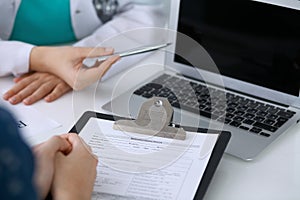 Close up of a doctor and patient sitting at the desk while physician pointing into laptop computer. Medicine and heal