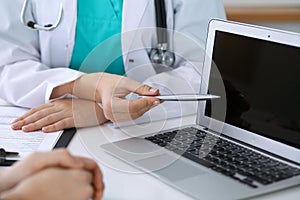 Close up of a doctor and patient sitting at the desk while physician pointing into laptop computer. Medicine and heal