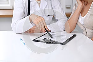 Close up of doctor and patient sitting at the desk while physician pointing into medical form hystory. Medicine a