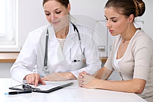 Close up of doctor and patient sitting at the desk while physician pointing into medical form hystory. Medicine a