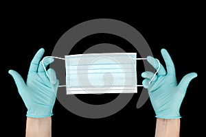 Close up of doctor`s hand in blue gloves with a medical face mask for protection against infection on black background. Covid.