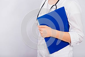 Close-up of a doctor`s hand holding a blue folder, a young woman in a white coat on a white background, copy space.