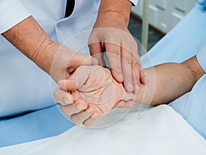 Close up doctor`s hand in white lab coat holding elderly patient`s hand who lying on the bed for checking examining heartbeat puls