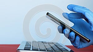 Close-up of a doctor`s hands in gloves with a computer keyboard phone. The doctor makes an important phone call. Smartphone in the