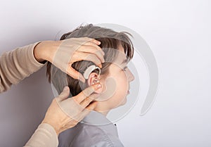 Close up of doctor`s hands inserting hearing aid in a youg boy patient`s ear