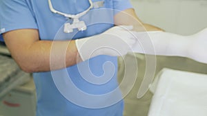 Close-up doctor in sterile clothing puts on gloves before surgery.