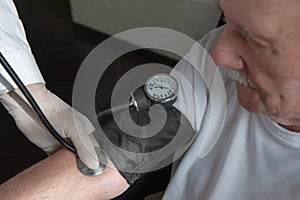 Close-up of a doctor using a stethoscope on an elderly person`s elbow to measure blood pressure. A gerontologist monitors the