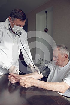 Close-up of a doctor using a stethoscope on an elderly person`s elbow to measure blood pressure. A gerontologist monitors the