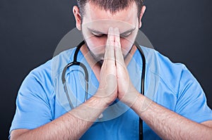 Close-up doctor wearing scrubs with stethoscope praying