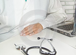 Close-up of a doctor in a white coat, calmly sitting at a table, with his hand on the table, against the background of a