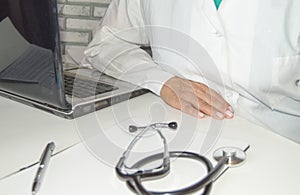 Close-up of a doctor in a white coat, calmly sitting at a table, with his hand on the table, against the background of a