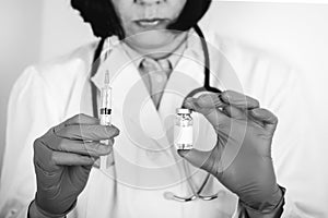 Close up of a doctor in white lab coat and sterile gloves holding syringe and medicine in ampoule photo