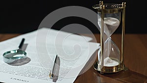 Close-up of document and hourglass on table, contract validity period expiring