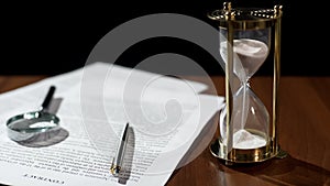 Close-up of document and hourglass on table, contract validity period expiring photo