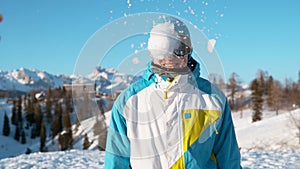 CLOSE UP: Stoked male snowboarder gets hit in the head by a large wet snowball. photo