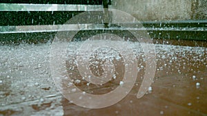 CLOSE UP: Tiny grains of soft hail fall on the wet brown floor of a balcony