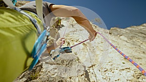 CLOSE UP, DOF: Young man belays a friend climbing high up a challenging wall.