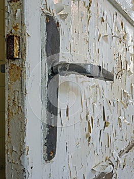 Close-up of door handle of old door with peeling white paint