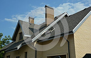 A close-up of a double complex roof of a brick house construction covered with gray asphalt shingles, fascia and soffit, with an