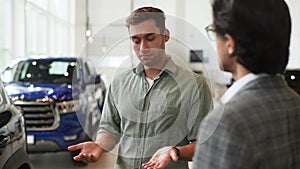 Close-up of doubtful male customer buying car in showroom talking to sales agent in business suit looking at auto