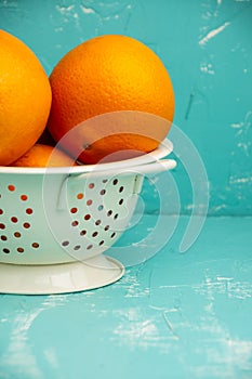 Close-up of drainer with oranges, selective focus, on table and blue background, in vertical