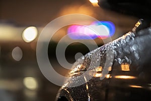 Close up of a dramatic black car at night, waiting in street lights in the heavy rain