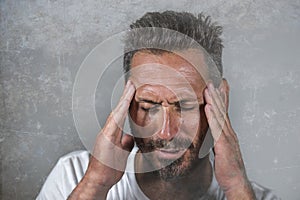 Close up dramatic  portrait of young attractive anxious and depressed man in pain with hands on his head suffering headache and