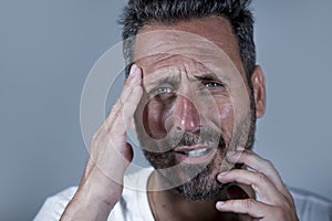 Close up dramatic  portrait of young attractive anxious and depressed man in pain with hands on his head suffering headache and