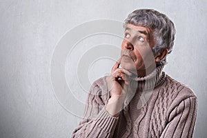 A close-up of dreamy elderly male holding his hand under chin looking aside having thoughtful faraway expression. Mature man daydr