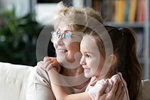 Close up dreamy smiling mature woman and granddaughter hugging