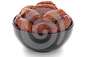 Close-up of dried date or chhuhara Phoenix dactylifera in a black ceramic bowl over white background