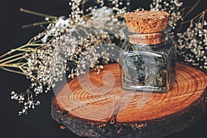 Close up of dried fireweed willowherb herbs in a square glass jar. Bottle on wooden tree trunk platform photo