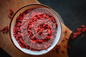 Close-up of dried goji berries in a bowl on dark background, top view