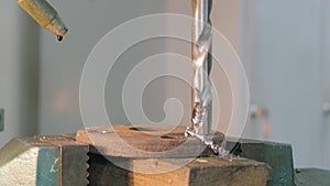 Close-up of a drill bit carving a hole into a metal part clamped down.
