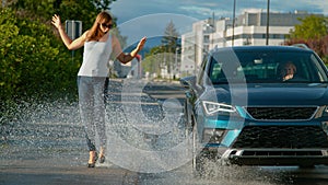 CLOSE UP: Driver drives her car into a puddle, splashing water at pedestrian.