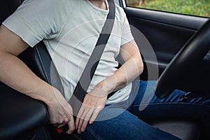 Close up driver fastening the seat belt. Person seated behind the steering wheel testing his new car safety. Secure transportation