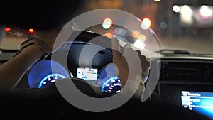 Close up of driver hands holding steering wheel driving car with blurred city street lights on background at night