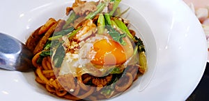 Close up dry Thai noodle with seafood, kale and yolk on top on white plate or dish.