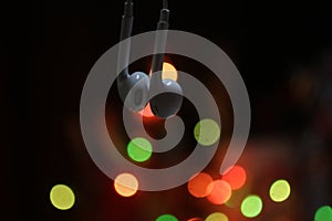 Close up of earphone hanging with colorful bokeh light on dark background. Copy space