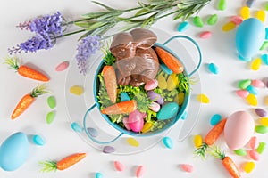 Close-up of Easter basket with chocolate bunny, mini carrots, and candy eggs on white background