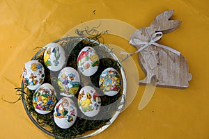 Close up on easter eggs and a wooden easter bunny on a yellow tablecloth with copy space