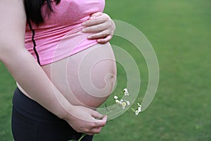 Close-up of Eastern Asian Chiense pregnant woman`s belly, flowers on belly, grass meadows as background in nature outdoor healthy