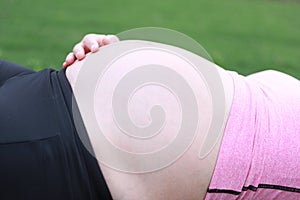 Close-up of Eastern Asian Chiense pregnant woman`s belly, lying on grass meadow field enjoy free casual time in nature outdoor