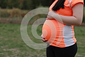 Close-up of Eastern Asian Chinese pregnant woman's belly, grass meadows as background, in forest garden outdoor nature